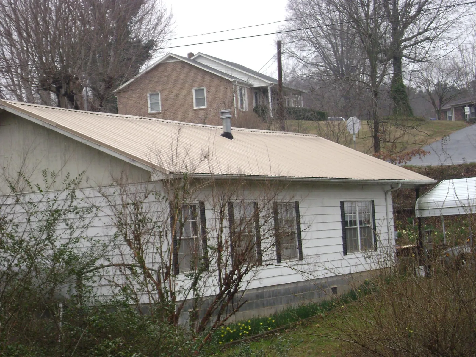Tan metal roof on a white sided house set into a hillside — Commercial Roofing by Roofing Brothers in Arcadia